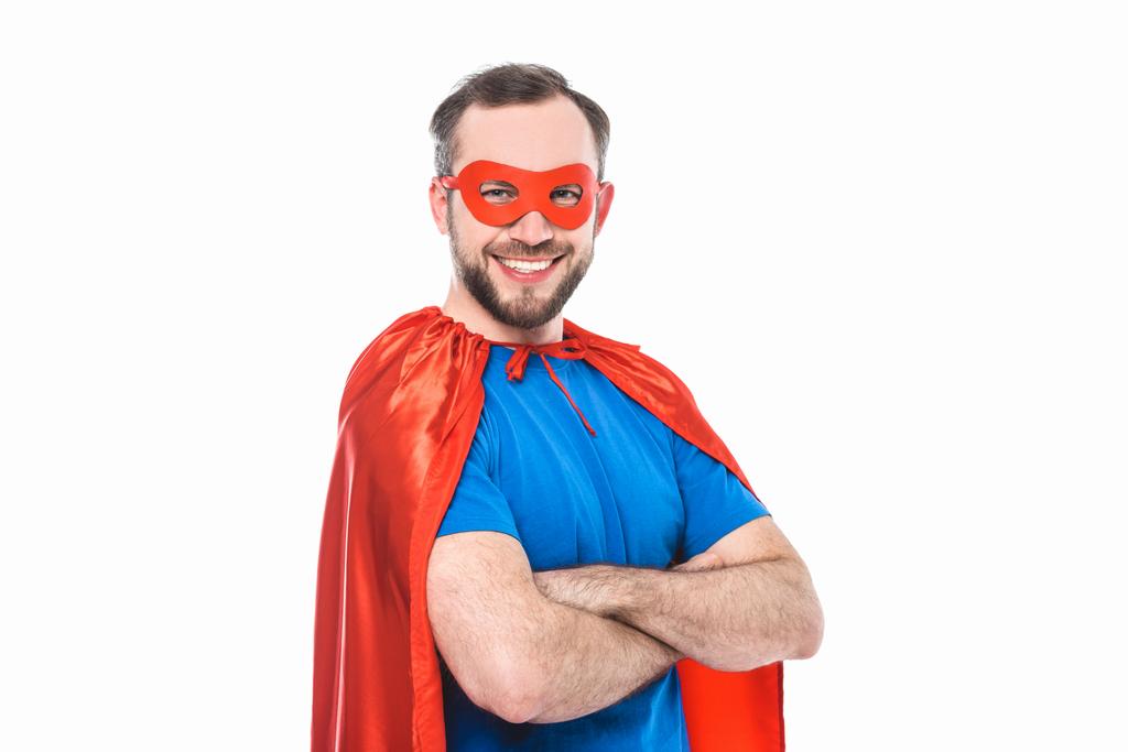 όμορφος γενειοφόρος άνδρας στο κοστούμι superhero στέκεται με σταυρωμένα χέρια και να χαμογελά στη φωτογραφική μηχανή που απομονώνονται σε λευκό - Φωτογραφία, εικόνα