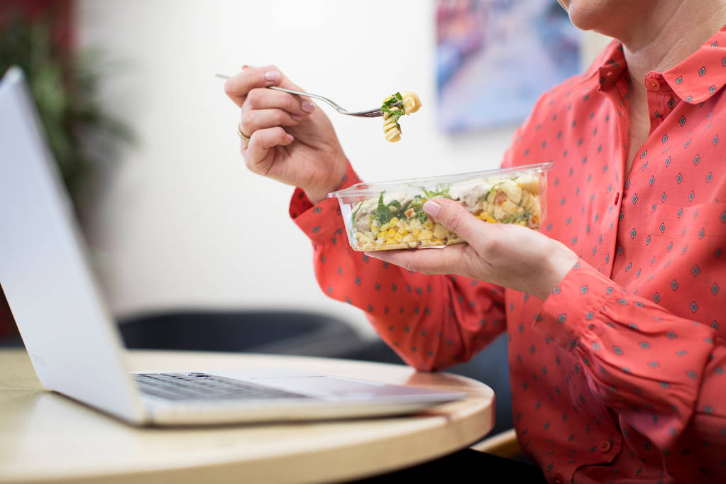 Vrouwelijke werknemer In kantoor met gezonde Pasta Lunch aan balie - Foto, afbeelding