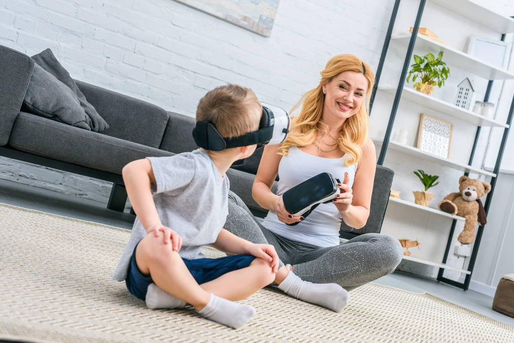Niño pequeño usando auriculares de realidad virtual y sentado con la madre
 - Foto, imagen