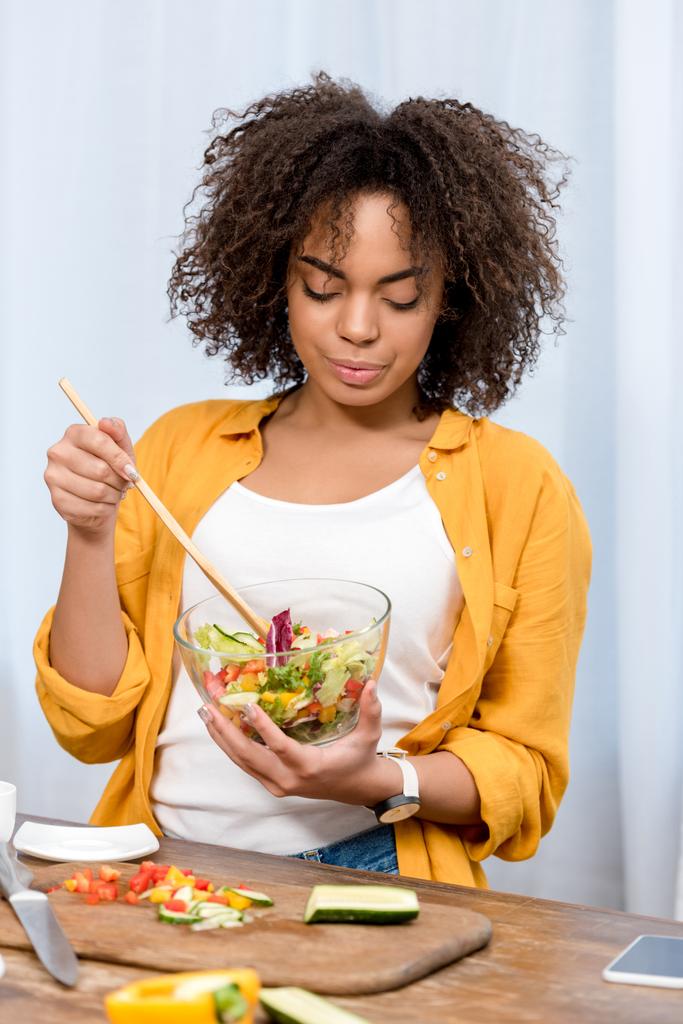 mooie jonge vrouw salade in kom mengen met houten spatel - Foto, afbeelding