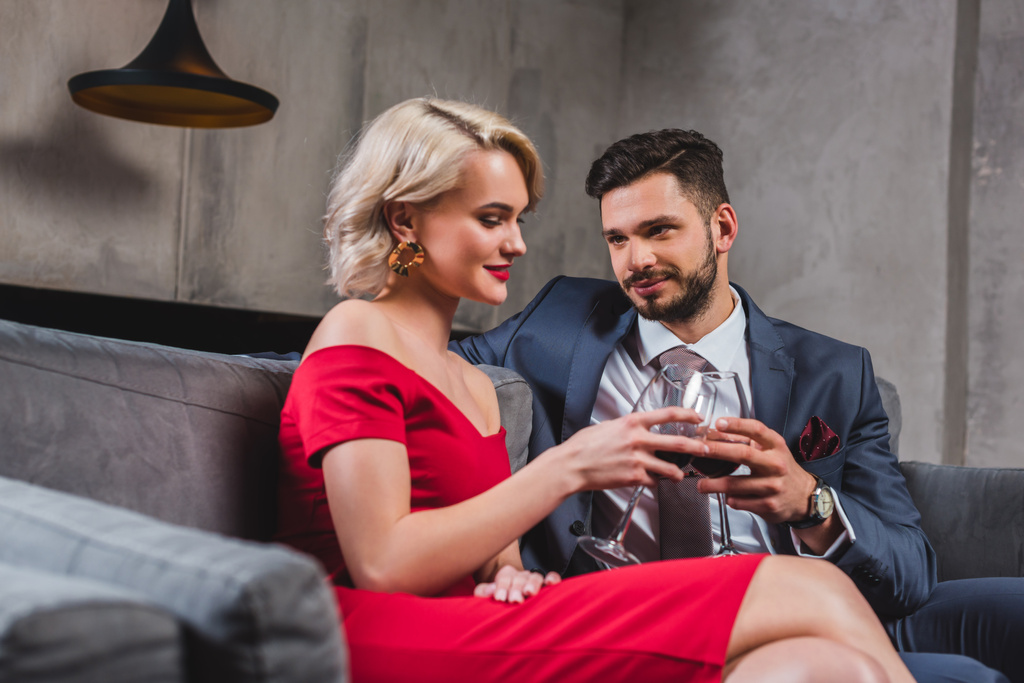 スーツとワインを一緒に飲みながら赤いドレスで美しいおしゃれなカップル  - 写真・画像