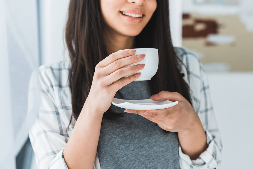 African american vrouw drinken koffie uit witte kop glimlachend - Foto, afbeelding