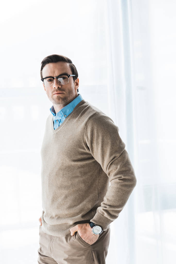Homem confiante vestindo roupas casuais e óculos em pé à janela
 - Foto, Imagem