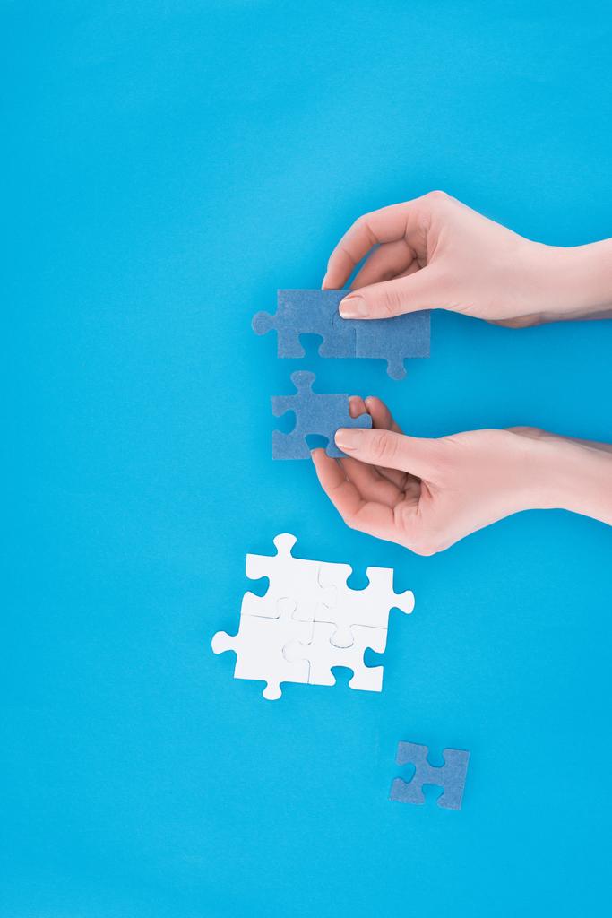 abgeschnittenes Bild einer Geschäftsfrau beim Zusammenbau blauer Puzzles auf blauem Grund, Geschäftskonzept - Foto, Bild