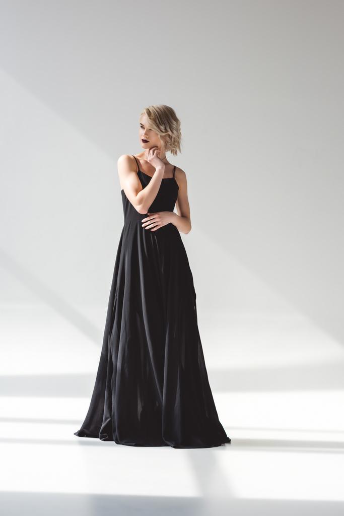 Blondynka młoda kobieta stwarzających w elegancka czarna sukienka, na szaro  - Zdjęcie, obraz