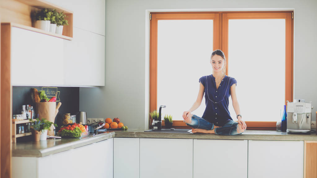 Молодая красивая женщина сидит за кухонным столом в позе лотоса
 - Фото, изображение
