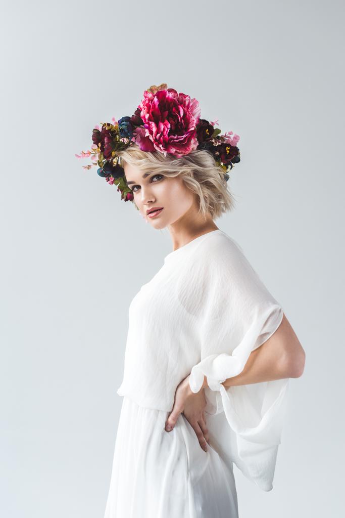 attractive blonde girl posing in white dress and floral wreath, isolated on grey - Photo, Image