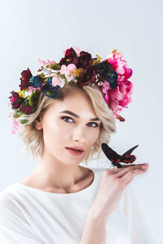 attractive girl posing in flower wreath with beautiful butterfly on hand, isolated on grey - Photo, Image