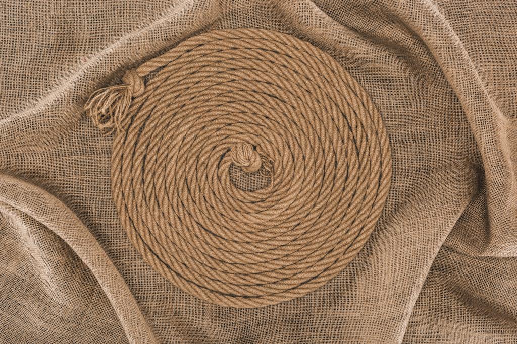 vista superior de la cuerda náutica marrón dispuesta en círculo sobre tela de saco
 - Foto, imagen