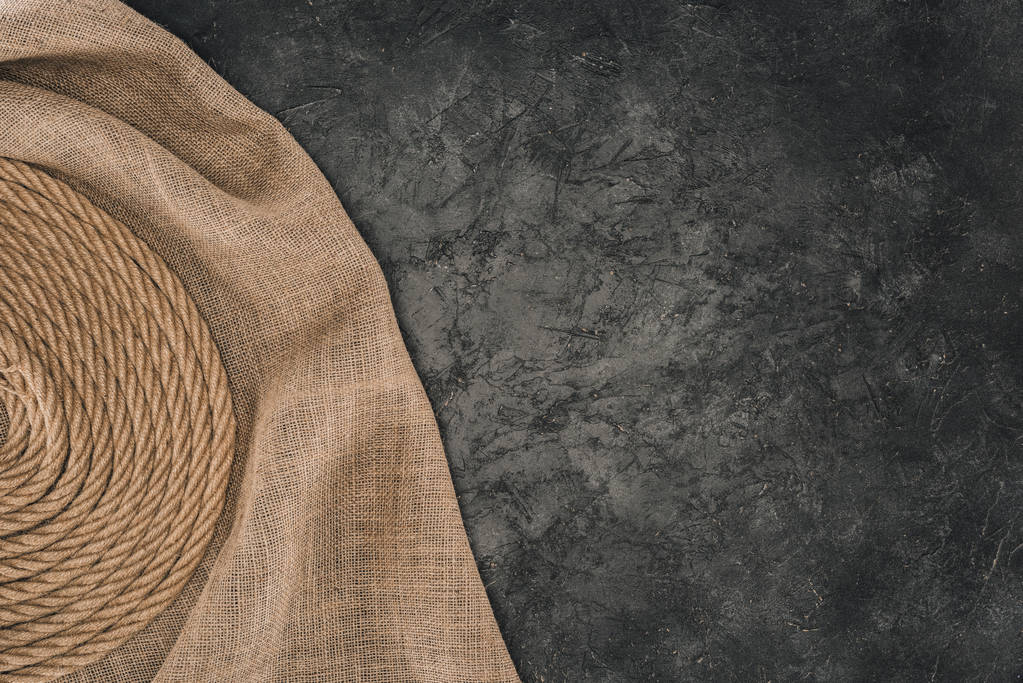 верхний вид коричневой морской верёвки, расположенной по кругу на мешковине на темно-бетонном столе
 - Фото, изображение