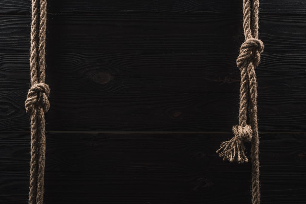 vista superior de disposición de cuerdas náuticas marrones con nudos sobre mesa de madera oscura
 - Foto, imagen