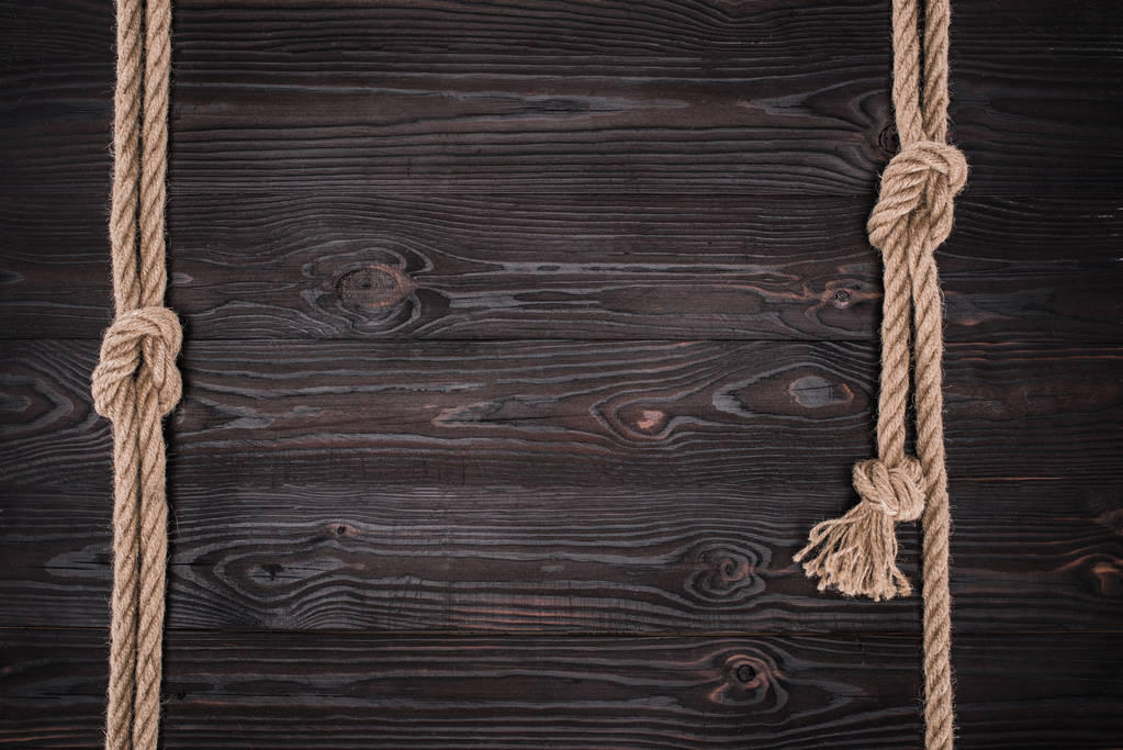 vista superior de arranjo de cordas náuticas marrons com nós em mesa de madeira escura
 - Foto, Imagem