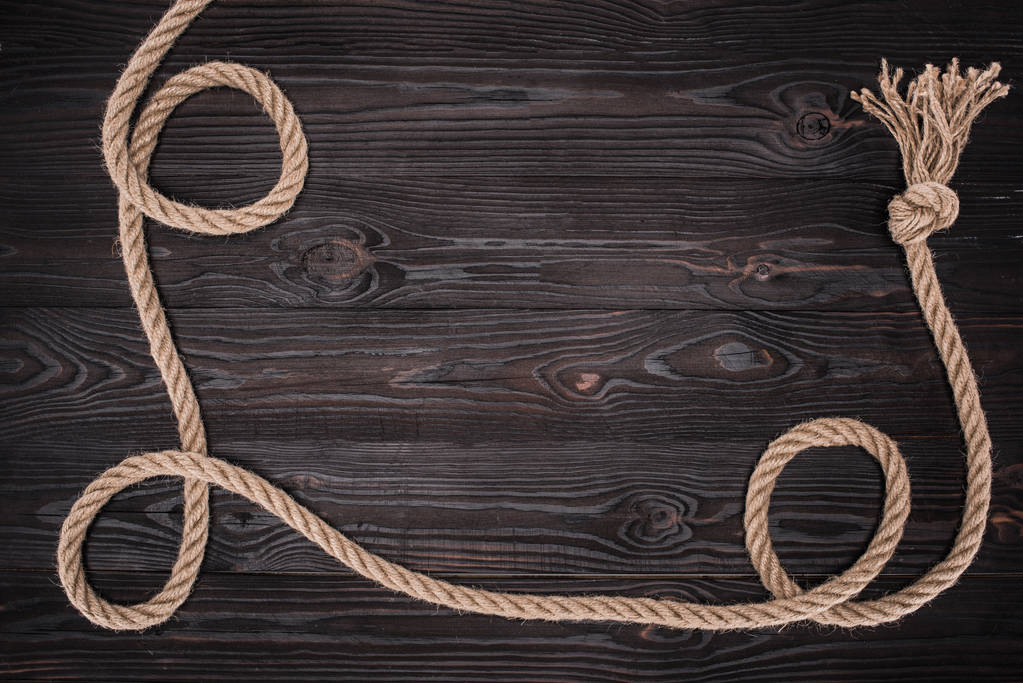 вид сверху на коричневую морскую верёвку с узлом на темной деревянной поверхности
 - Фото, изображение