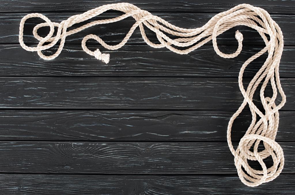 bovenaanzicht van gearrangeerde witte mariene touwen met knopen op donkere houten tafelblad - Foto, afbeelding