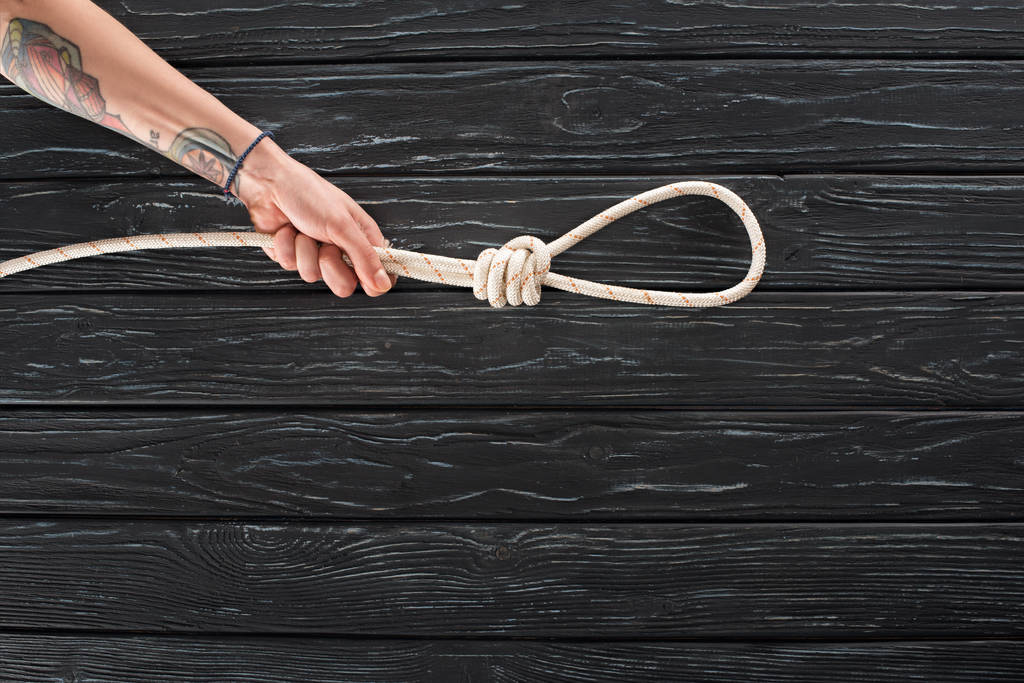 vista parziale della mano femminile con corda marina con nodo sulla superficie di legno scuro
 - Foto, immagini