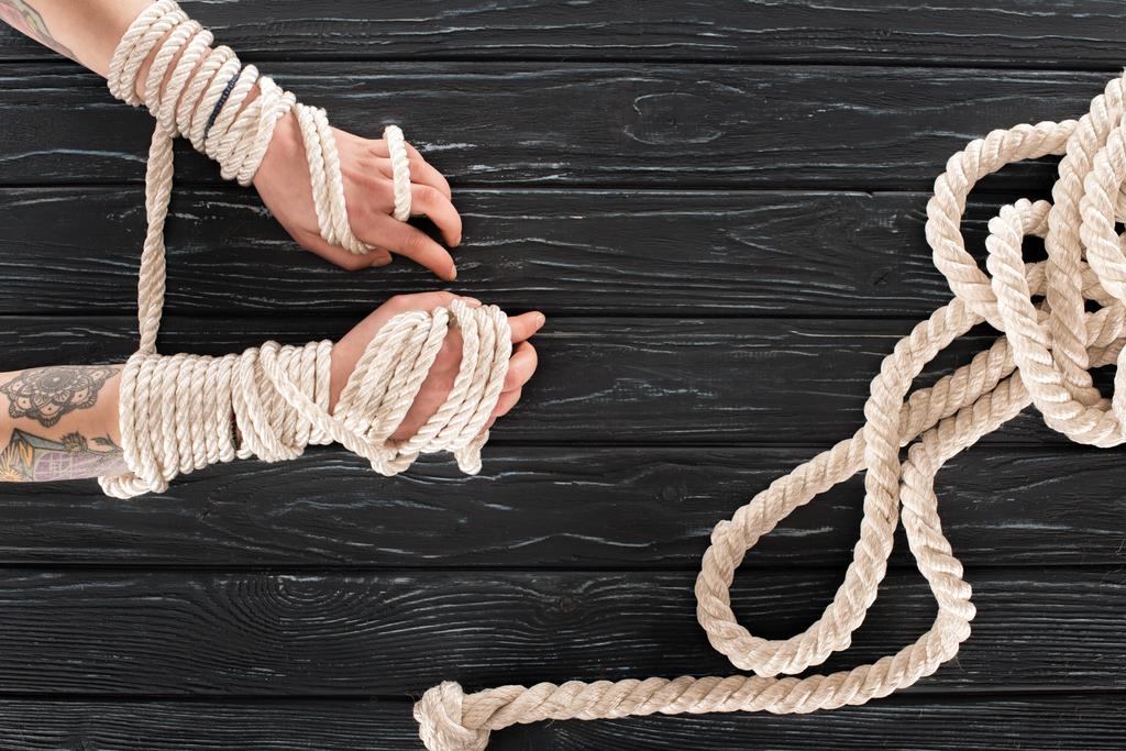 обрізаний знімок жіночих татуйованих рук, прив'язаних до мотузки на темній дерев'яній стільниці
 - Фото, зображення