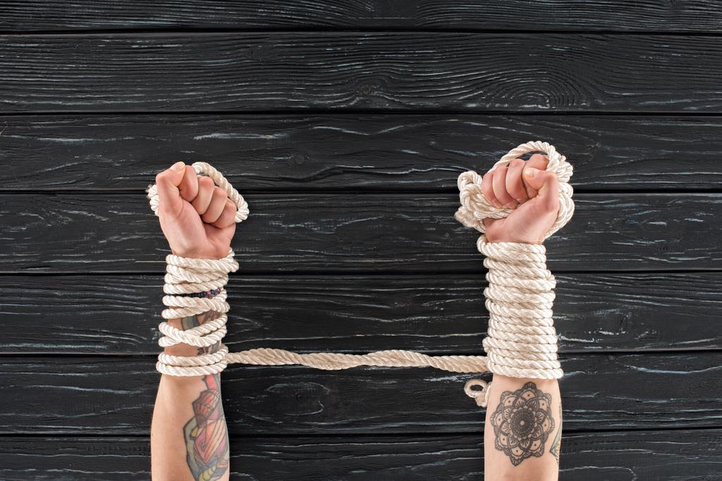 cropped shot of female tattooed hands tied in rope on dark wooden tabletop - Photo, Image
