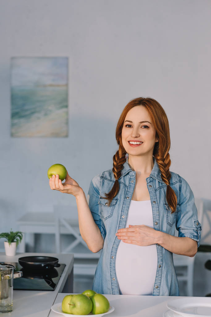 mosolygó terhes nő mutatja az apple konyha - Fotó, kép