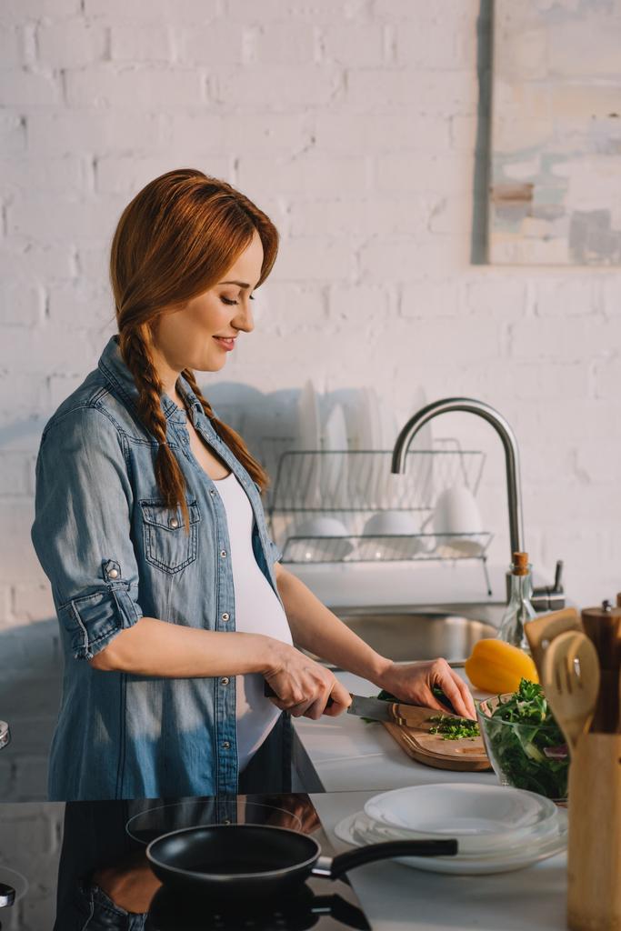 vista lateral de la atractiva mujer embarazada preparando ensalada en la cocina
 - Foto, imagen