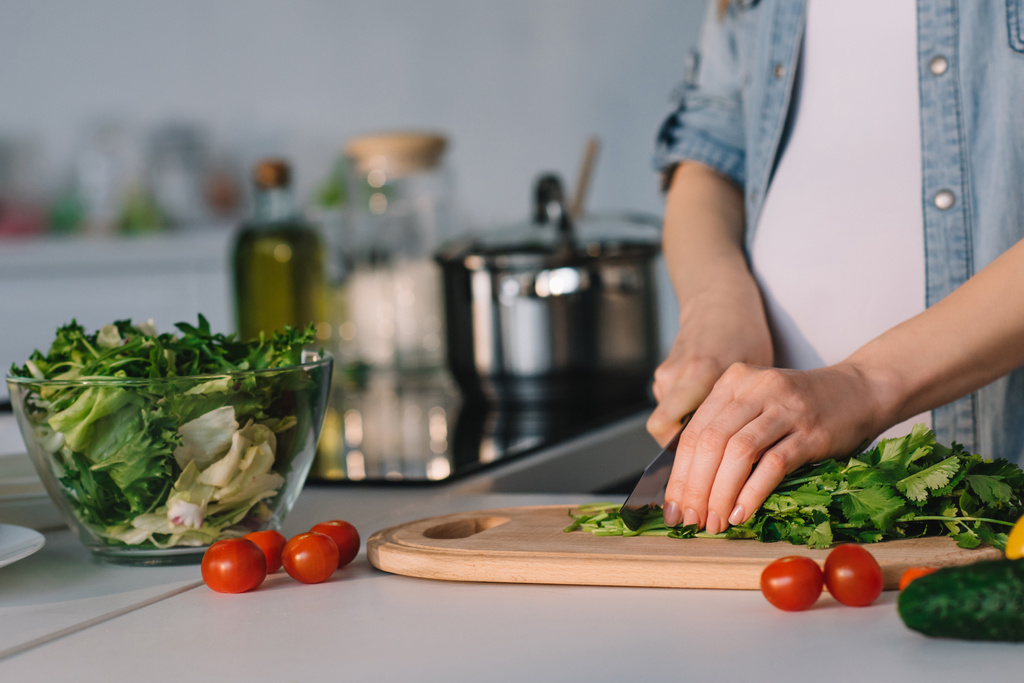 imagen recortada de mujer embarazada atractiva cortando verduras para ensalada en la cocina
 - Foto, Imagen