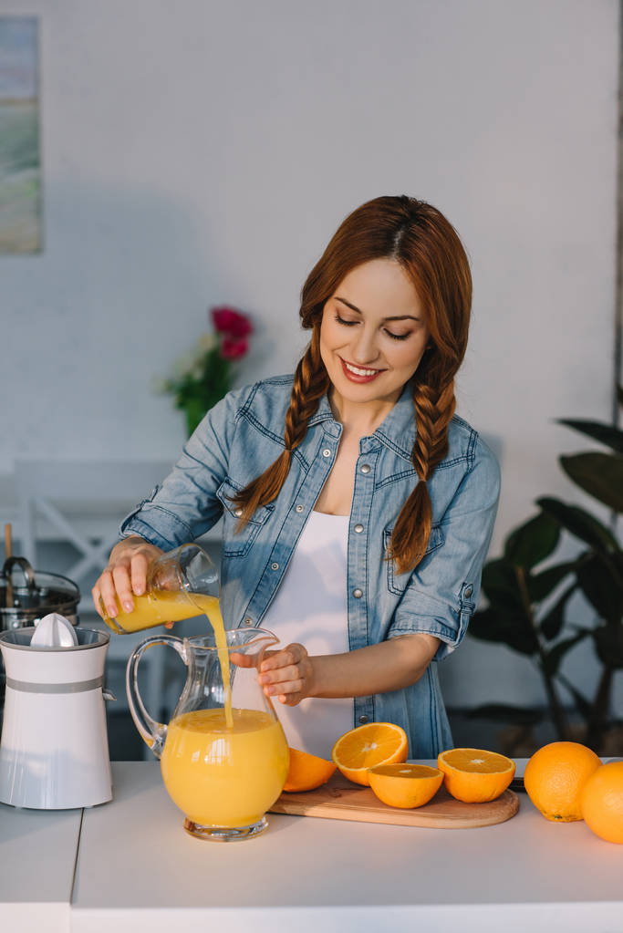 ελκυστική έγκυος γυναίκα ρίχνει χυμό πορτοκαλιού σε κανάτα στην κουζίνα - Φωτογραφία, εικόνα