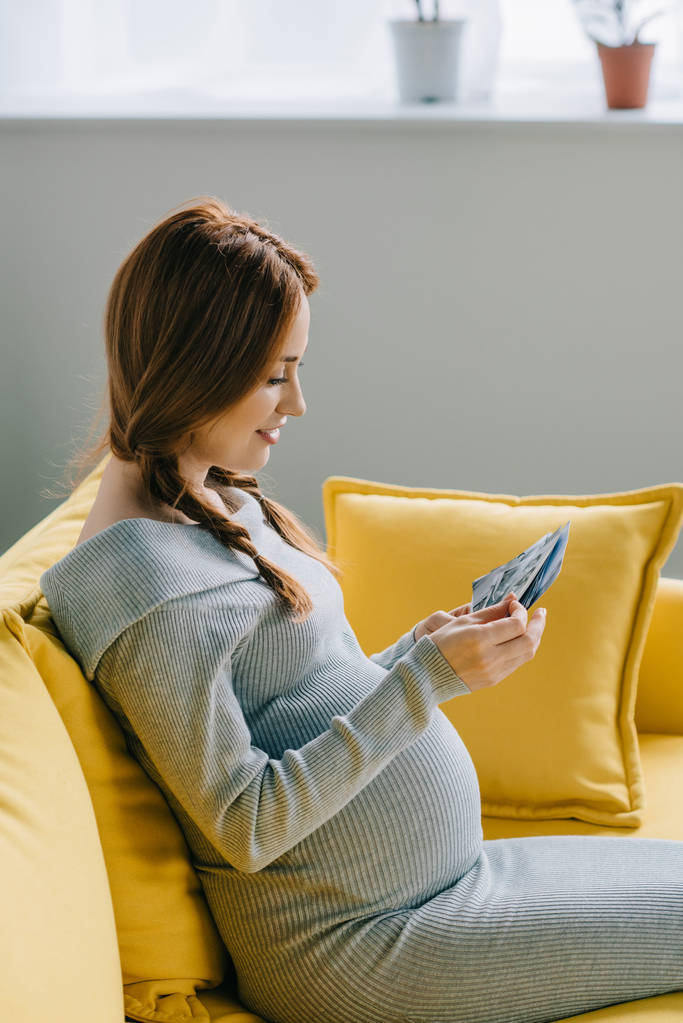 vista laterale di attraente donna incinta guardando le foto in soggiorno
 - Foto, immagini