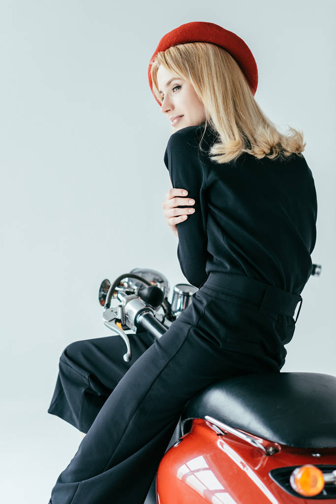 Attractive young woman in black clothes posing by red motorcycle isolated on grey - Photo, Image
