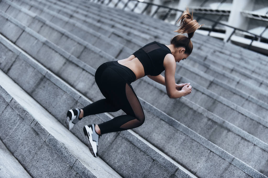 Moderni nuori nainen urheilu vaatteet hyppäämällä harjoitellessaan ulkona
 - Valokuva, kuva