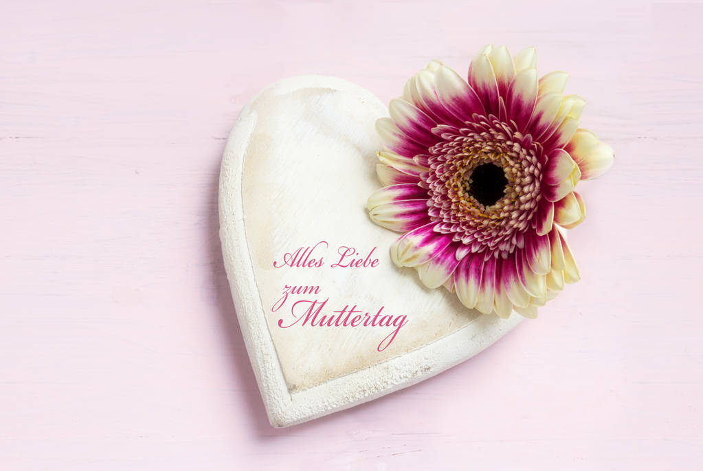 white painted wooden heart shape and a flower head on a bright pink background, german text Alles Liebe zum Muttertag, meaning Happy Mother's Day, top view from above with copy space - Photo, Image