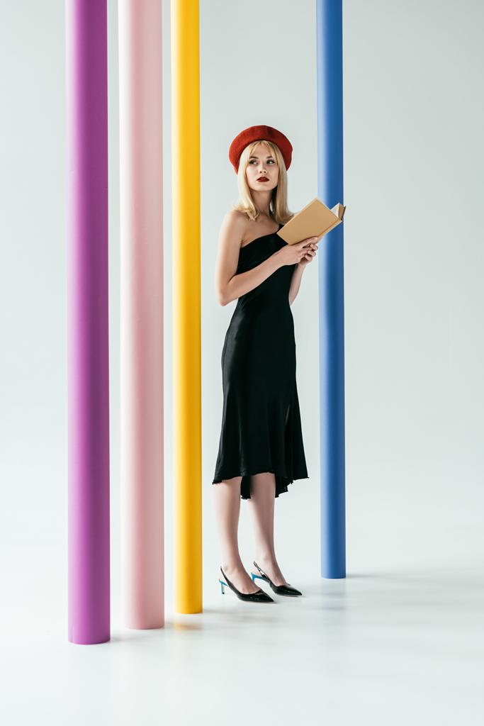 Aantrekkelijke jonge vrouw in zwarte jurk bedrijf boek door kleurrijke pijlers - Foto, afbeelding