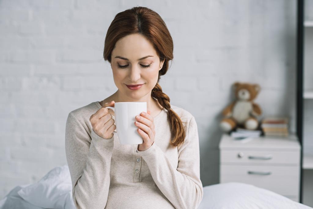 szép terhes nő gazdaság csésze tea szoba - Fotó, kép