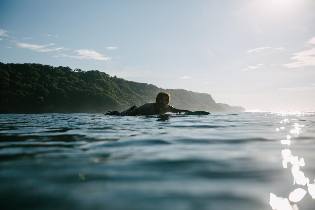 Красивый мужчина плавает на доске для серфинга в солнечный день
 - Фото, изображение