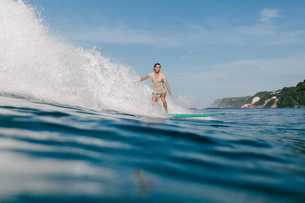 Zijaanzicht van de jongeman in natte t-shirt paardrijden golven op een surfplank terwijl het hebben van vakantie - Foto, afbeelding