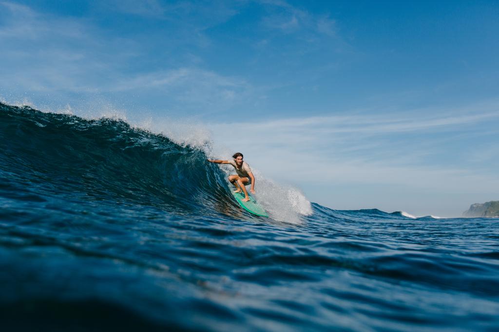 professionele surfer in natte t-shirt paardrijden golven op een surfplank op zonnige dag - Foto, afbeelding