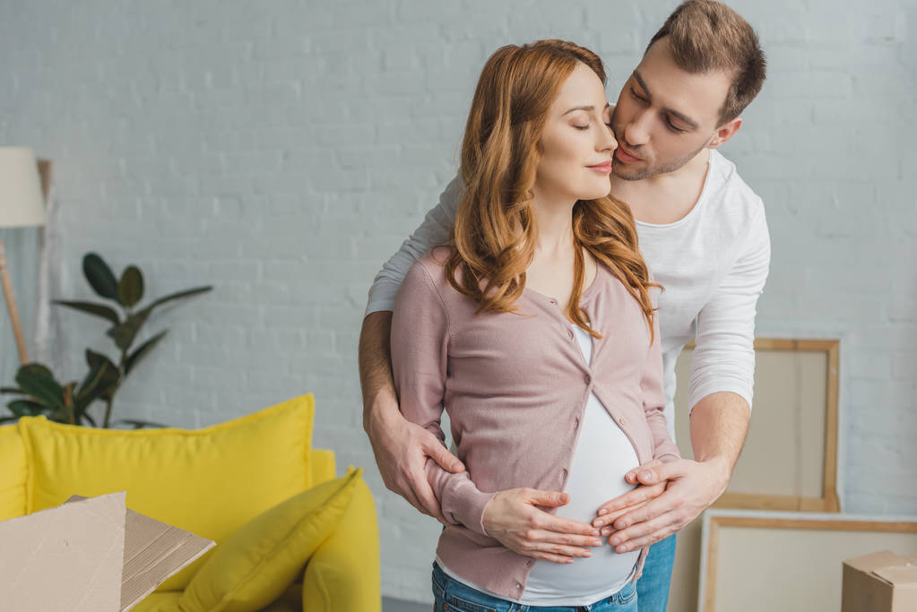 молодой человек обнимает и целует счастливую беременную женщину в новой квартире
 - Фото, изображение