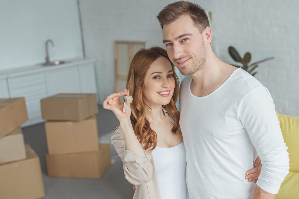 счастливая молодая пара держит ключ от новой квартиры и улыбается на камеру
 - Фото, изображение