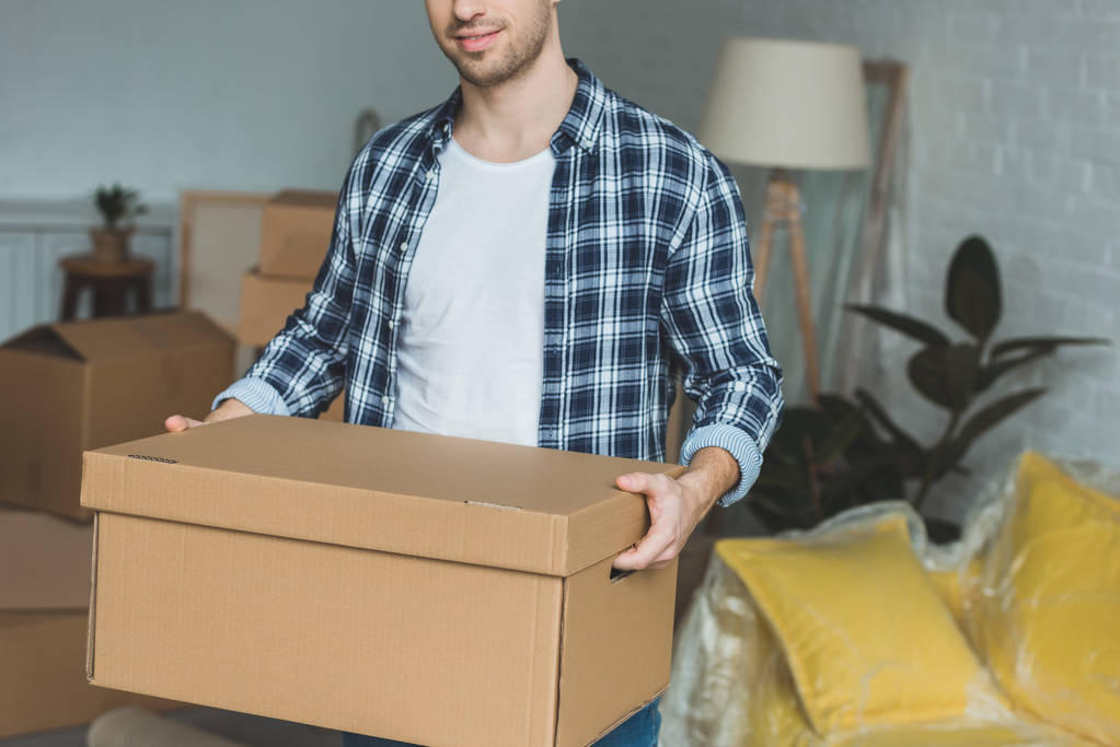 vista parcial del hombre con caja de cartón en las manos en el nuevo hogar, concepto de reubicación
 - Foto, imagen