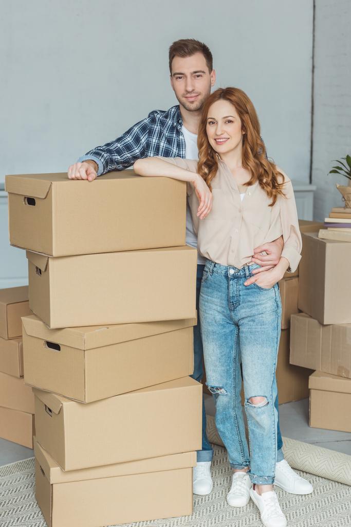 smiling couple leaning on pile of cardboard boxes at new home, relocation concept - Photo, Image