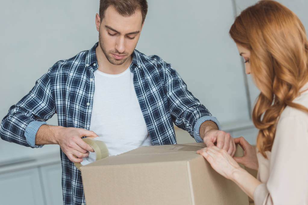 couple packing cardboard box with sticky tape together, relocation concept - Photo, Image