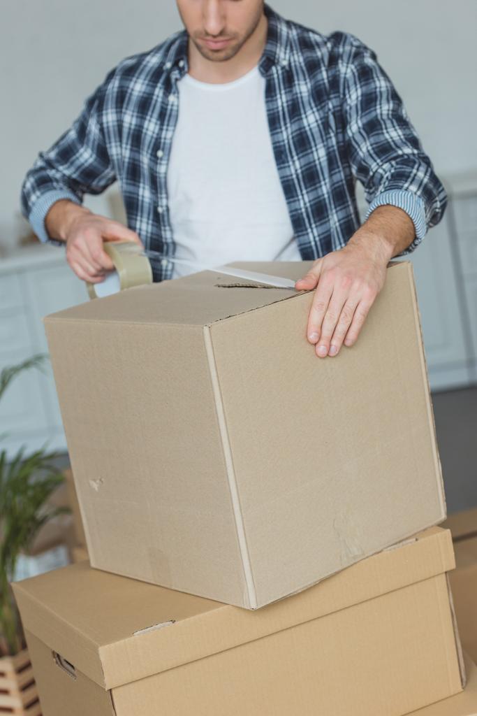 Teilansicht von Mann beim Packen von Karton mit Klebeband, Umzugskonzept - Foto, Bild