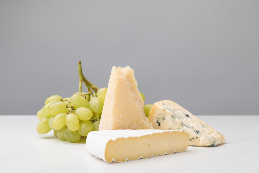 Closeup view of three types of cheese and grapes on gray  - Photo, Image
