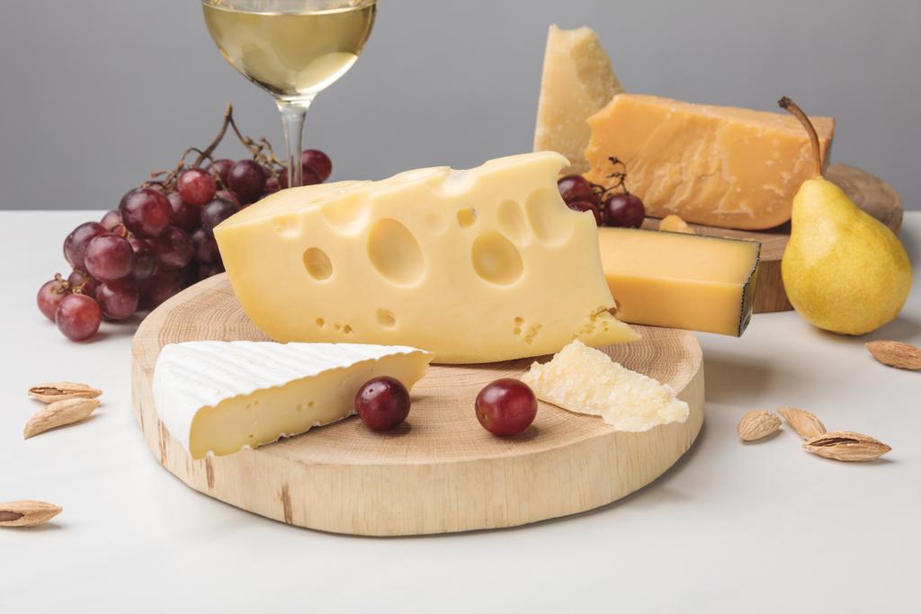 Différents types de fromage sur des planches en bois, verre à vin, fruits et amande sur gris
 - Photo, image