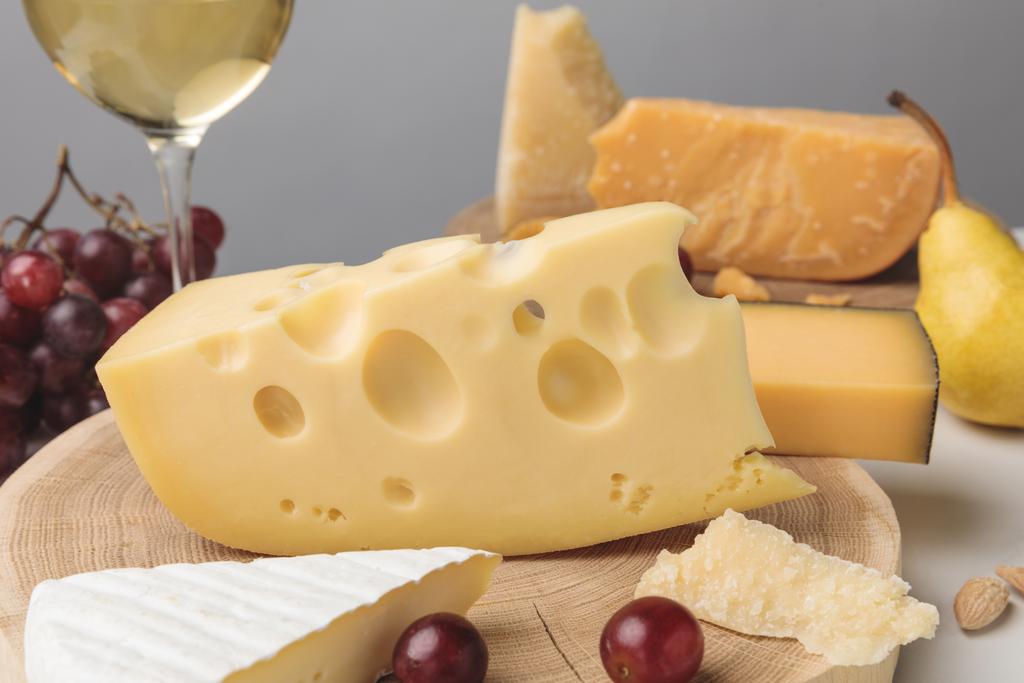 Closeup shot of different types of cheese on wooden board, pear, grapes and wine glass on gray - Photo, Image