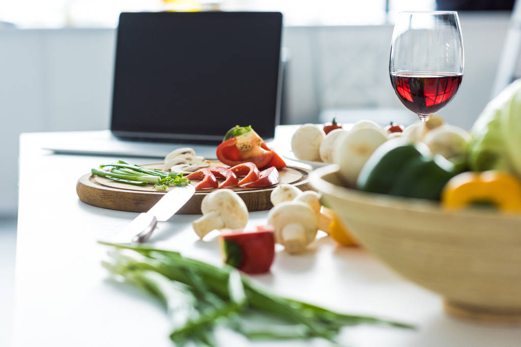 dizüstü bilgisayar, kadeh kırmızı şarap ve mutfak masasının üzerinde sebze - Fotoğraf, Görsel