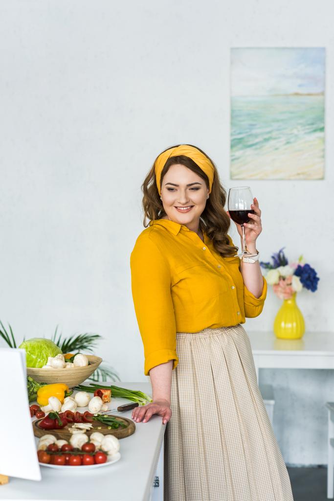 mooie vrouw houdt van glas wijn en groenten in de keuken kijken - Foto, afbeelding