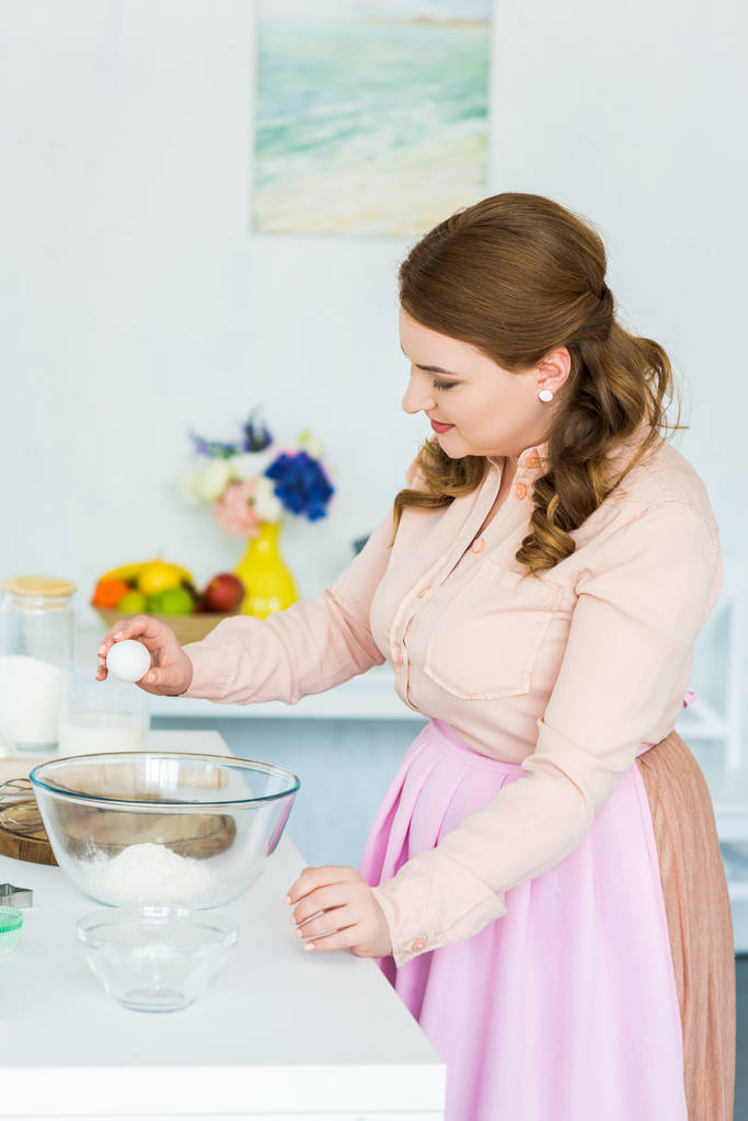 vista lateral da bela mulher quebrando ovo para massa de farinha na cozinha
 - Foto, Imagem