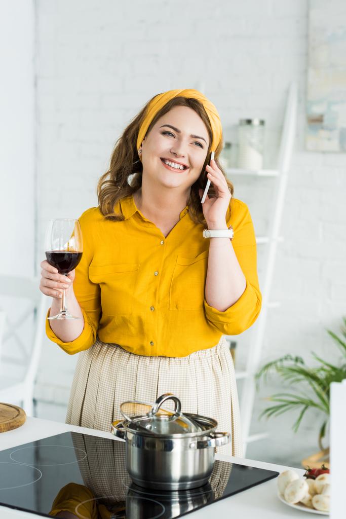 mujer hablando por teléfono inteligente y beber vino en la cocina
 - Foto, Imagen