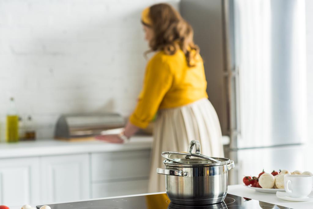 žena vaření v kuchyni pan na elektrický sporák na popředí - Fotografie, Obrázek