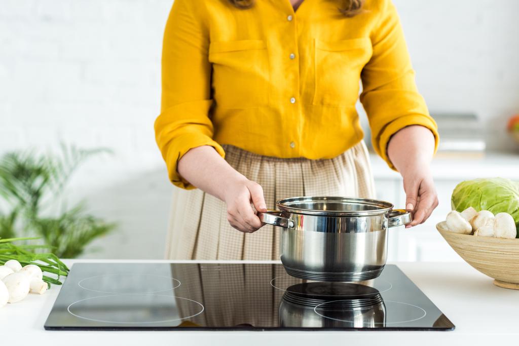 bijgesneden afbeelding van vrouw zetten pan op elektrisch fornuis in de keuken - Foto, afbeelding