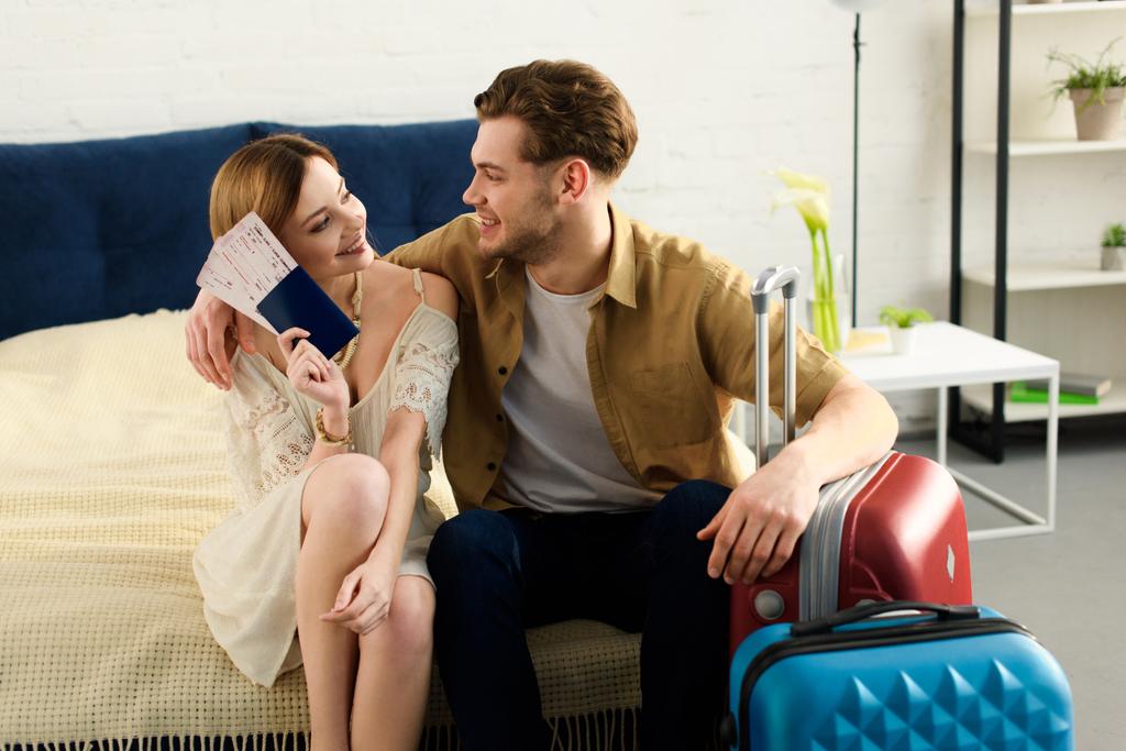 glimlachend paar met koffers op bed en kaartjes met paspoorten te houden - Foto, afbeelding